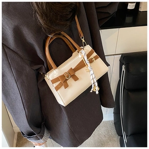 Detail einer beige-braunen Mini-Umhängetasche mit Schleife und Schlüsselanhänger am Modell