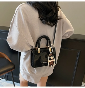 Detail of black glossy leather crossbody bag with braided handle and cute plush charm