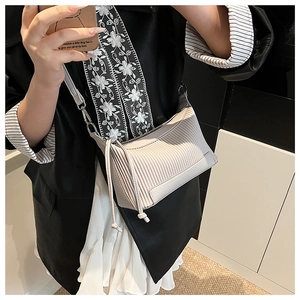 Détail d'un sac beige avec design plissé, texture litchi et pompons longs élégants