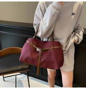 Detail of burgundy tote bag with leather trim and silver buckle on shoulder