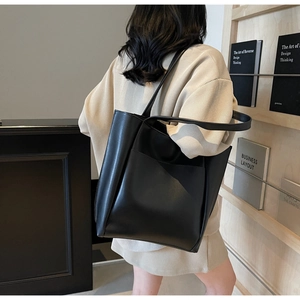 Detail of minimalist black tote bag with front pocket shown on shoulder in office setting