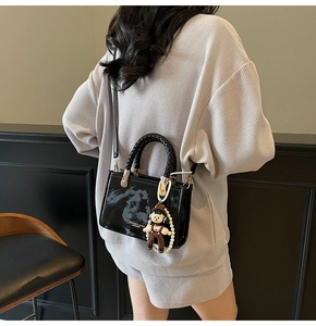 Detail view of black patent leather crossbody bag with astronaut doll and pearl chain