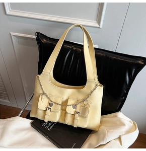 Close-up of pale yellow tote bag with dual front pockets and silver heart chain detail