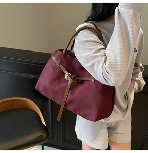 Detail of burgundy large capacity tote bag with leather trim and round metal buckle