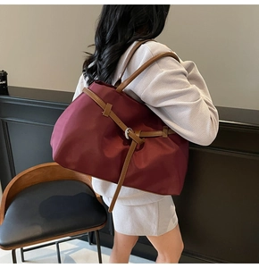 Detail view of large burgundy tote bag with leather straps on model's shoulder