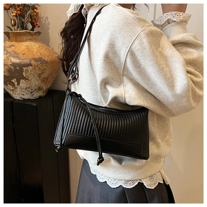Détail du sac bandoulière noir avec texture ondulée et nœuds latéraux sur un mannequin