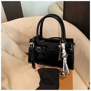 Detail einer schwarzen glänzenden Handtasche mit Bogenschnalle, Seidenschal und Goldanhänger