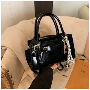 Detail einer schwarzen Lackleder-Handtasche mit goldener Schnalle und gestreiftem Seidenschal