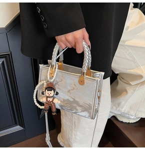 Detail of silver metallic tote with woven handles and a cute doll charm accessory