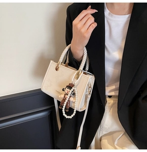 Detail of cream leather handbag with woven handle, pearl chain, and fashion lettering