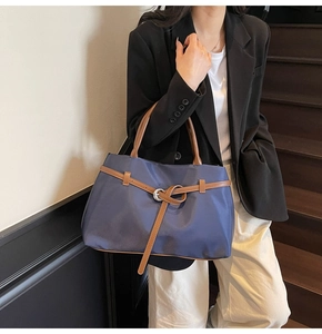 Close-up of a large navy nylon tote bag with brown leather handles worn by a model