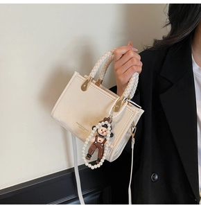 Detail of cream white leather square handbag with woven handle and pearl charm