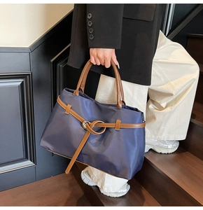 Detail of the navy blue nylon tote bag with brown leather handles and decorative belt