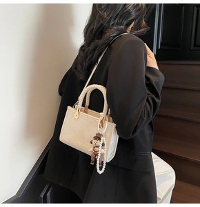 Detail of cream square handbag with woven handles and cute doll pearl charm accessory