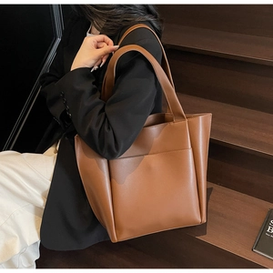 Detail shot of a brown leather tote bag on model showing large capacity and flat straps