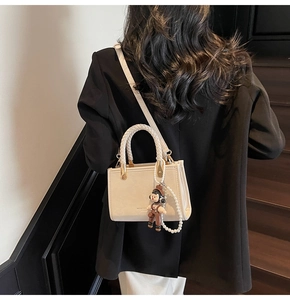 Detail of off-white crossbody bag with woven handle and cute doll charm accessory