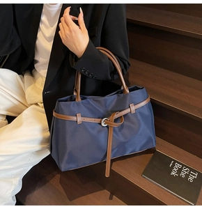 Detail view of dark blue nylon tote bag with brown leather handles and buckle decoration
