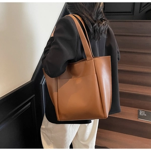 Brown leather tote bag featuring a large front pocket shown on a model in a minimalist setting