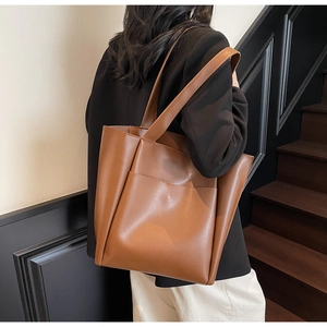 Detailed view of a retro brown leather tote bag worn by a model in a modern indoor setting
