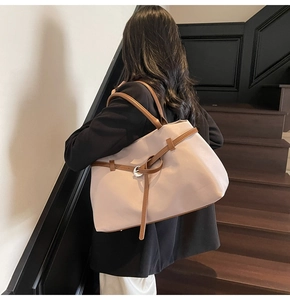 Detailed back view of a beige minimalist tote bag with leather straps on a wooden staircase