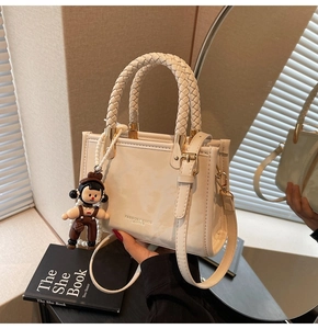 Detail of cream leather handbag with woven handle and cute doll charm pendant