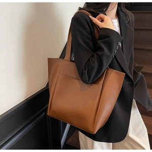 Brown leather tote bag featuring a spacious interior and minimalist shoulder strap design