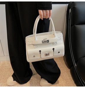 Detail view of white leather handbag with classic metal twist locks and functional pockets