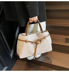 Detail of large beige nylon tote bag with brown leather handles held by a model