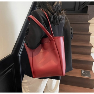 Detailed view of deep red matte leather tote bag with large front pocket on wooden stairs