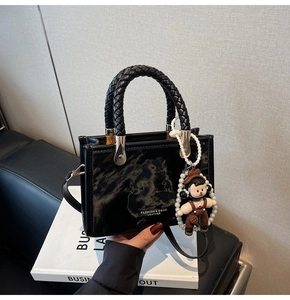 Detail of black marble textured handbag with woven handle and cute doll charm accessory