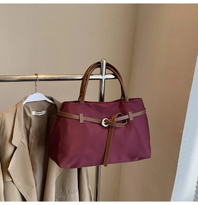 Detail of burgundy tote bag showing nylon texture and brown leather strap with metal buckle