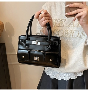Detail of black glossy handbag featuring three front pockets and silver twist-lock closures