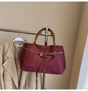 Detail of burgundy tote bag with brown leather strap and silver buckle on a trench coat