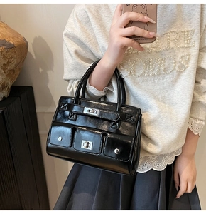 Close-up of black glossy handbag with silver rotary locks and three flap pockets