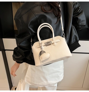 Dettaglio borsa beige in pelle a grana di litchi con chiusura a scatto e ciondolo a cuore