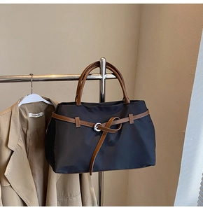 Detail of black nylon tote bag featuring brown leather handles and silver ring buckle