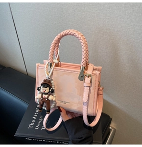 Pink crossbody bag with woven handle and cute doll charm on a leather background