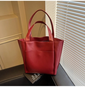 Detail of deep red leather tote bag with front pocket resting on a leather seat