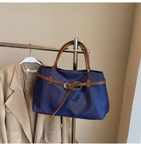 Detail of dark blue nylon tote bag with brown leather handles and belt buckle decor