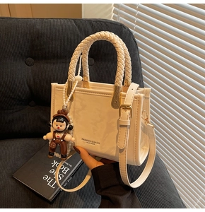 Detail of a creamy white crossbody bag with a woven handle and cute doll accessory