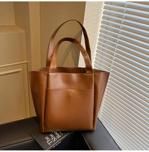 Detail of a brown leather tote bag with large front pocket on a black leather bench