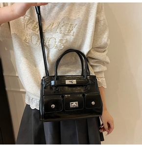 Detail of black patent leather handbag with metal buckle and functional pockets on a model