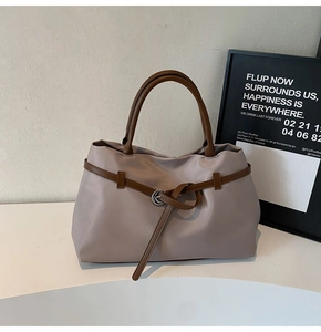 Detail of grey-purple tote bag showing contrast brown straps and polished buckle