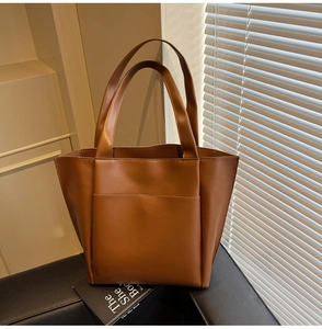 Close-up of brown faux leather tote bag with large front pocket and dual handles on black stand