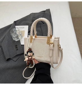 Detail of cream leather mini handbag with woven handle and cute doll charm on suit fabric