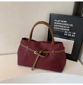 Close-up of burgundy tote bag with brown leather handles and silver ring buckle detail