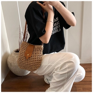 Close-up detail of the woven straw bag featuring brown leather strap and gold button closure