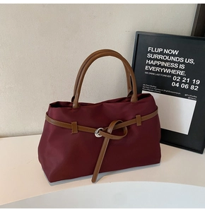 Detailed macro view of deep red tote bag with brown leather handles and buckle accent