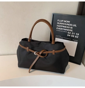 Close-up of large black tote bag with brown leather handles and silver buckle details