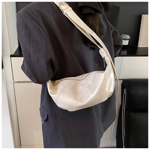 Detail of cream-colored dumpling bag featuring curved quilted stitching and wide strap